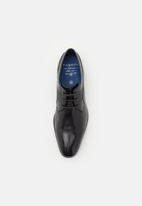 Chaussure habillée en cuir noir avec un bout pointu et une texture lisse. Elle comporte deux œillets pour les lacets et une semelle intérieure bleue avec un logo.