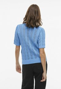 Suéter de punto azul claro de manga corta con un patrón de encaje texturizado y dobladillo acanalado, hecho de material suave. Vista trasera.