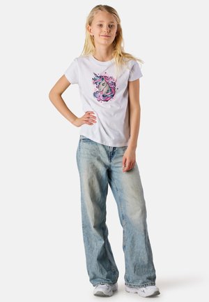 White cotton t-shirt with a unicorn graphic in pink and blue, paired with light blue baggy denim jeans and white sneakers.