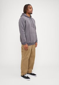 Grå bomull hettegenser med frontlomme, svarte snorer, kombinert med beige cargo-bukser og svarte joggesko med hvite såler.