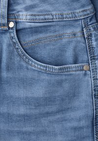 Close-up of blue denim jeans showing the front pocket with visible stitching and metal rivets on seams and belt loop.