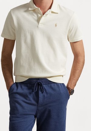 Kremowa koszulka polo z kołnierzykiem i małym logo na lewej piersi, w zestawie z granatowymi spodniami dresowymi na sznurki.