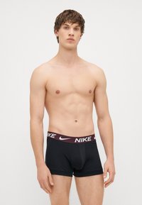 Μαύρα σλιπάκια μποξέρ με μπορντό ζώνη που φέρει το λογότυπο "NIKE" σε λευκό χρώμα. Το ύφασμα φαίνεται λείο με εφαρμοστό σχέδιο.
