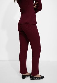 Burgundowa, prążkowana bluzka i spodnie o teksturowanym wykończeniu. Spodnie mają surowy brzeg. Czarne baleriny z srebrnymi ćwiekami dopełniają strój.