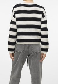 Chunky stickad tröja med horisontella svartvita ränder, ribbade ärmslut och lös passform, tillsammans med högmidjade grå jeans.