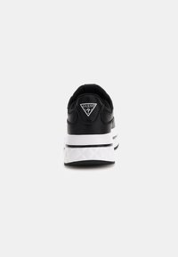 Sneaker nera con tomaia in pelle texturizzata, suola piatta bianca e patch a logo triangolare sul tallone. Finitura liscia, design low-top.