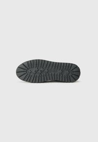 Semelle extérieure en caoutchouc noir avec des crampons profonds et un bout arrondi. Présente une surface texturée et un détail de logo en relief près du talon.