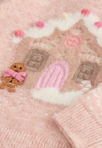 Rosa gestrickter Pullover mit einem Design von einem Lebkuchenhaus, bestickt in Braun und Rosa mit flauschigen weißen Akzenten und bunten Pompons.