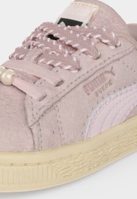 Κοντινή λήψη ενός ανοιχτό ροζ τζούντ sneaker της Puma με πλεκτά κορδόνια, κρεμ σόλα και λογότυπο Puma στο πλάι και στη γλώσσα.