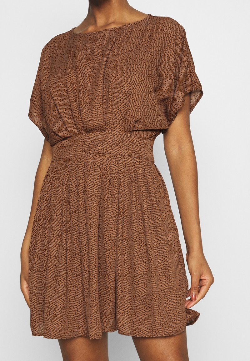 Robe marron à motif avec une coupe ample, des manches courtes et une taille cintrée, présentant une jupe évasée et un tissu doux et texturé.