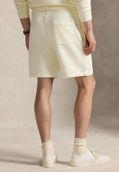 Šviesiai geltonos trumpikės su laisvu kirpimu, su viena atgaline kišene ir minkšta medžiaga. Derinamos su baltais sportbačiais ir kreminėmis kojinėmis.