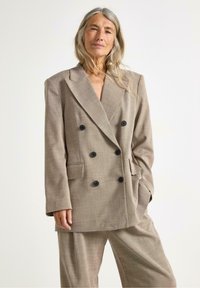 Dobbeltradet blazer i lysebrunt stof med en subtil tekstur, der har store sorte knapper og skrå lommer. Skræddersyet pasform.