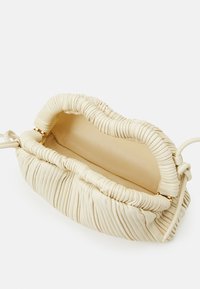 Krémová kožená kabelka s nařasenou texturou, zlatou hardware a jedním ramenním popruhem. Otevřené vnitřní prosvětlení ukazuje hladkou podšívku.