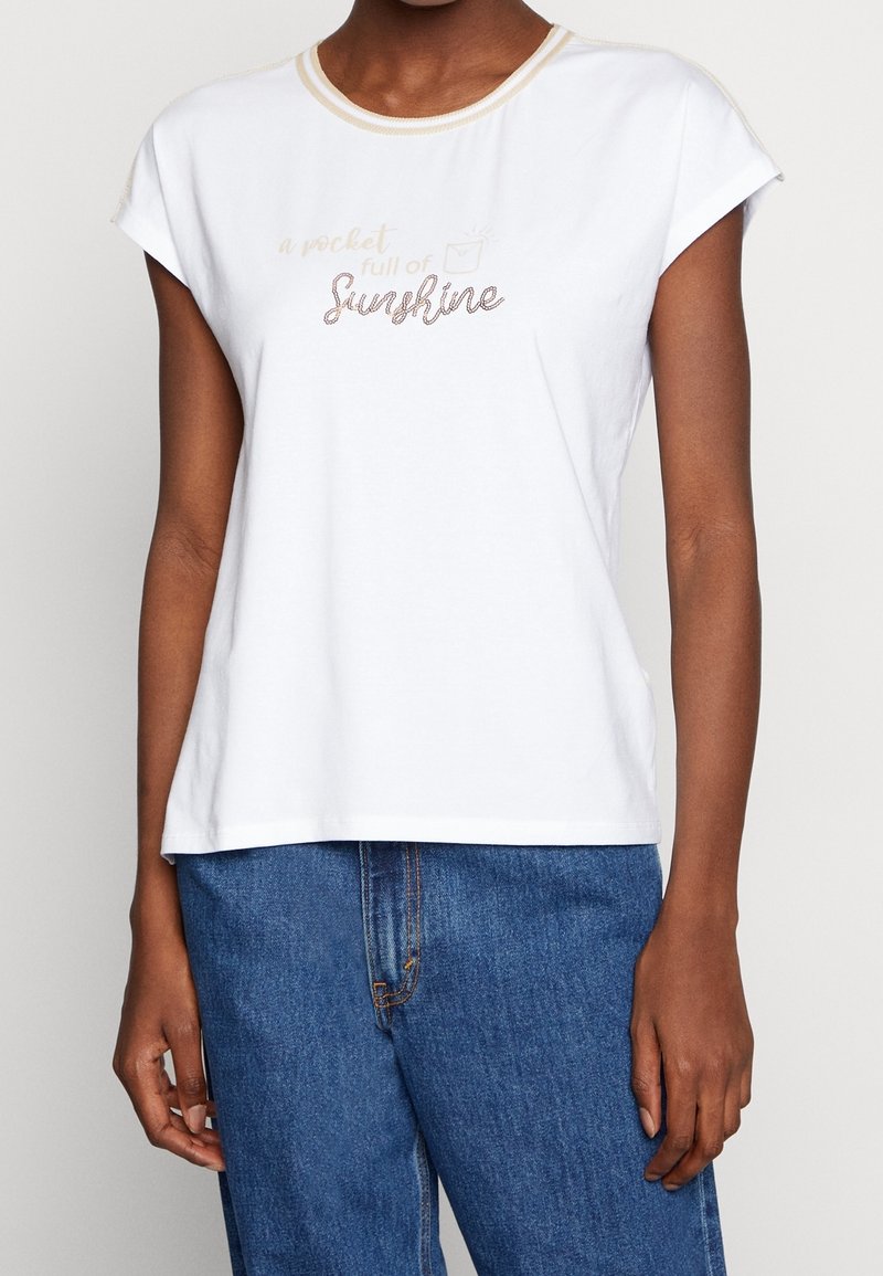 Hvid bomulds t-shirt med korte ærmer, der har en guldfarvet halsudskæring og trykt tekst "en lomme fuld af solskin" i en dekorativ skrifttype.