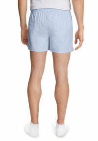 Shorts en coton bleu clair avec une taille élastique, coupe droite et texture subtile. Portés avec des chaussettes blanches mi-mollet.