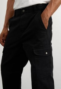 Μαύρο παντελόνι cargo με χαλαρή εφαρμογή, διαθέτει πλευρικές και μπροστινές τσέπες, μπροστινό κούμπωμα και μαλακό βαμβακερό ύφασμα. Ιδανικό για ευέλικτους συνδυασμούς.