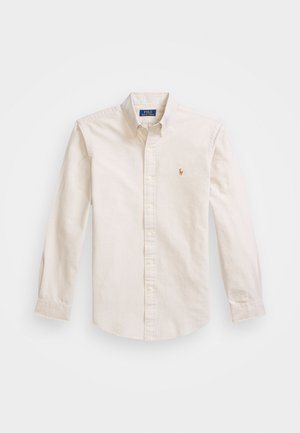 Chemise beige à boutons en tissu coton, avec un col pointu, des manches longues et un logo brodé sur la poitrine.