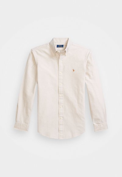 Beige button-up shirt in cotton fabric, featuring a pointed collar, long sleeves, and an embroidered logo on the chest.