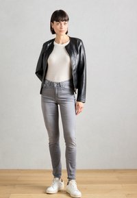 Svart skinnjakke med en tettsittende design, hvit ribbestrikket topp, grå slim-fit jeans og hvite joggesko. Glatt tekstur og minimalt med maskinvare.