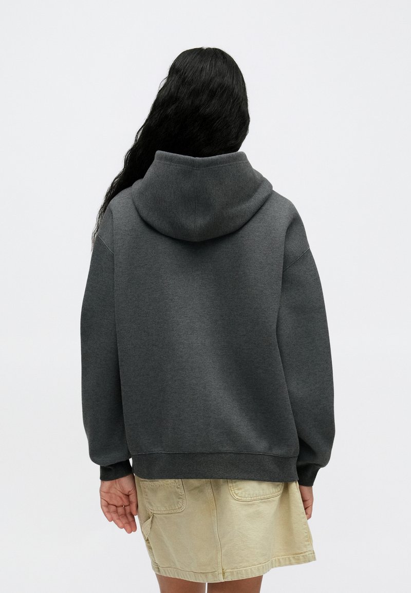 Mørkegrå hættetrøje med en afslappet pasform og en stor hætte. Fremstillet i tekstureret stof med drop-skulder og ribbede manchetter. Nederdelen er beige.