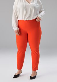 Rote, eng anliegende Hosen aus elastischem Stoff, mit glatter Textur und zulaufenden Beinen, kombiniert mit einer lockeren, weißen Bluse mit Kordelzügen.