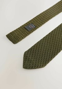 Woven zielony krawat z teksturowanym wzorem, spiczastym końcem i małą czarną metką z informacjami o marce w pobliżu wąskiego końca.