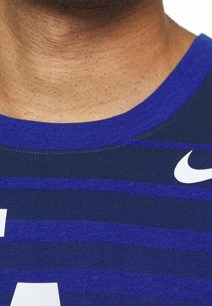 Tummansininen urheilupaita, jossa on vaakasuoria raitoja eri sävyissä sinistä, ja edessä valkoinen Nike-logo. Pehmeä kangas.