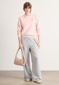 Ljusrosa sweatshirt med ribbad mudd och rundad hals; kombinerad med löst sittande grå mjukisbyxor och en liten beige handväska.