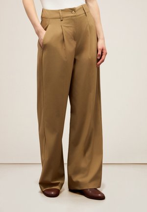 Pantaloni a gamba larga in tessuto beige, con pieghe frontali, tasche inclinate e chiusura con un bottone in vita. Texture liscia.