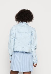 Ljus tvättad denimjacka med en cropped passform, fransat avslut och subtila broderade mönster. Långa ärmar och klassisk kragdesign.