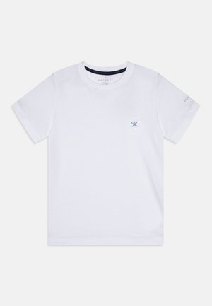 Bílá krátká trička s krátkým rukávem vyrobená z bavlny. Obsahuje malé modré logo na levé straně hrudi a výšivku "HACKETT" na pravém rukávu.