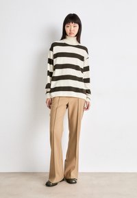 Beige og mørkegrønne stripete genser med høy hals, kombinert med beige skräddersydde bukser og mørkegrønne sko. Enkel og moderne design.