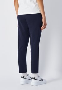 Granatowe dresy wykonane z miękkiego materiału, o zwężanym kroju, w połączeniu z białymi trampkami. Widoczne szwy i ściągacze na mankietach.