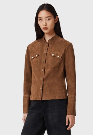 Camicia in suede marrone con chiusura a bottoni a pressione, due tasche sul petto e colletto a punta. Finitura testurizzata con una silhouette aderente.