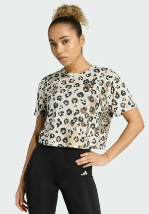 T-shirt beige cropped con macchie di leopardo nere e marroni. Tessuto morbido con scollo tondo e maniche corte, abbinato a leggings neri.