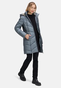 Gray puffer coat with a hood, diamond quilted pattern, front zipper, side pockets, and faux fur trim. Worn with black top and pants.