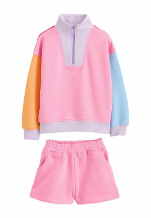 Dvojdielny detský outfit s ružovou mikinou na zips, ktorá má jeden oranžový a jeden modrý rukáv, doplnený ružovými šortkami s elastickým pásom.