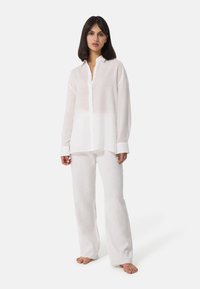 Camicia bianca a maniche lunghe con colletto, chiusura con bottoni frontale e texture trasparente, abbinata a pantaloni larghi in lino bianco. Design semplice e minimalista.