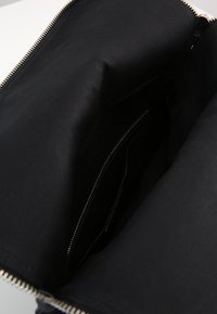 Interno di una borsa a tracolla in tessuto nero con una texture liscia e una tasca con zip. Presenta una zip metallica lungo il bordo superiore.