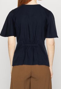 Top blu navy a maniche corte con vita arricciata e tessuto morbido. La parte posteriore presenta un semplice scollo rotondo e discreti dettagli di cucitura.
