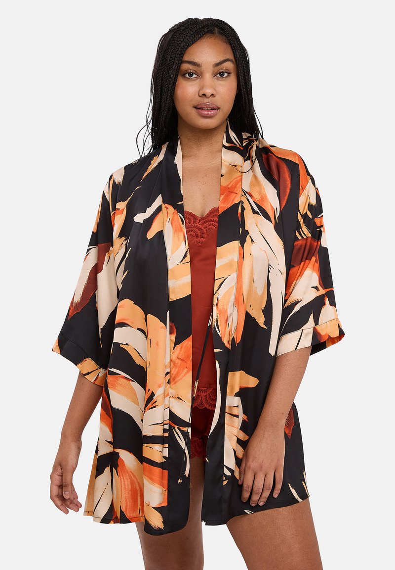 Femme avec des cheveux tressés portant une robe kimono noire ornée de grands imprimés floraux orange et beige sur de la lingerie avec des bordures en dentelle couleur rouille.