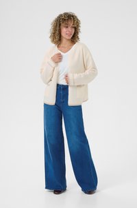 Cardigan ivory cu o croială lejeră, dintr-un amestec de lână, cu mâneci largi și două buzunare frontale. Este combinat cu blugi blue cu talie înaltă și croială largă.