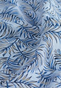 Baumwollstoff mit einem hellblauen Hintergrund, der ein Muster aus Palmenblättern in Dunkelblau und Beige zeigt. Weiche Textur mit subtiler glänzender Oberfläche.