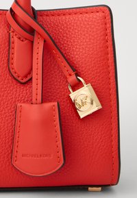 Borsa a tracolla in pelle rossa con superficie testurizzata, dotata di un lucchetto in oro con logo MK, tracolla in pelle coordinata e bordi neri a contrasto.