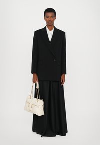 Μαύρο oversized σακάκι, λευκό πουκάμισο, μακριά μαύρη φούστα και ανοιχτόχρωμη τσάντα με αλυσίδες. Λείο ύφασμα, δομημένη σιλουέτα.