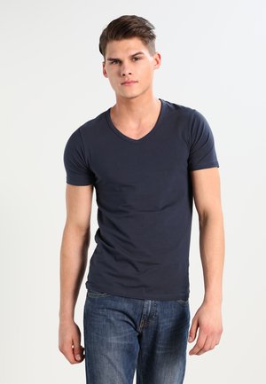 T-shirt bleu marine à col en V en coton, avec des manches courtes et une coupe ajustée, associé à un jean en denim bleu.