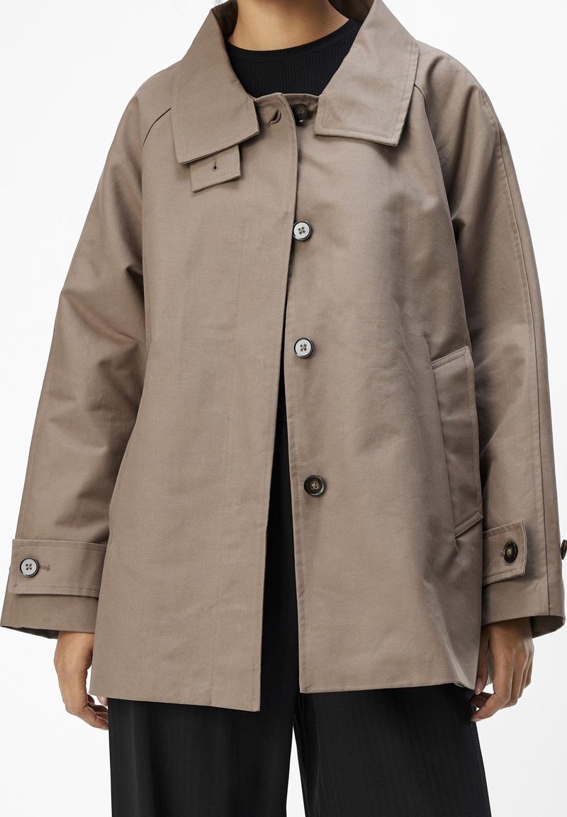 Chaqueta de algodón color coñac con cuello con solapas, botones frontales y bolsillos laterales. Corte holgado con puños abotonados y detalles de diseño mínimos.