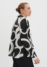 Camicia a maniche lunghe in bianco e nero con un audace motivo circolare astratto. Realizzata in tessuto leggero, presenta un fit morbido e spacchi laterali.