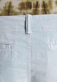 Ljusblå denimbyxor visade bakifrån, med en kort midja, två bakfickor och en slät yta.