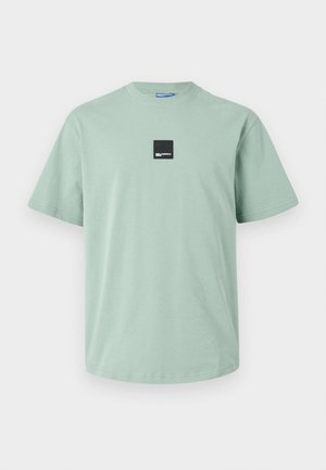 Mintgroene katoenen t-shirt met korte mouwen, ronde hals en een klein zwart vierkant logo-embleem op de voorkant. Soepele textuur, relaxte pasvorm.